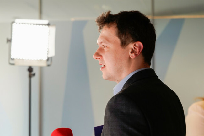 Harris wearing a shirt and suit jacket speaking beside a microphone with a light behind him.